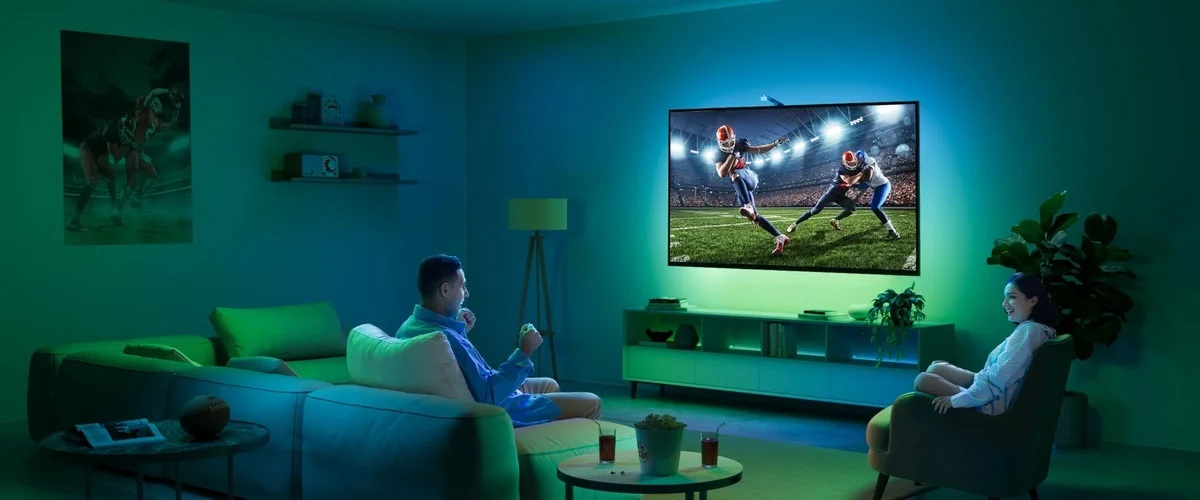 Mężczyzna i kobieta oglądają mecz w telewizji w pokoju z zielonymi światłami.