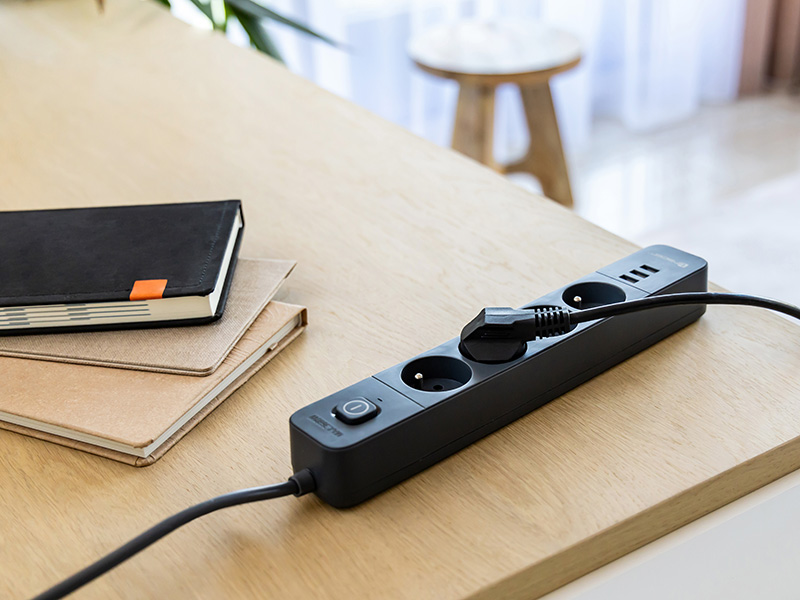 Listwa zasilająca z trzema gniazdami i przyciskiem zasilania na biurku.