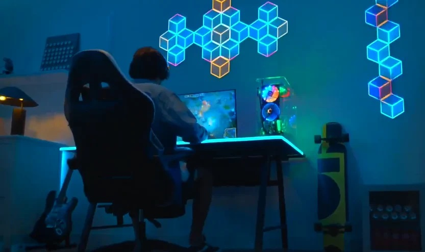 Osoba grająca na biurku z komputerem i podświetlanym wzorem na ścianie.