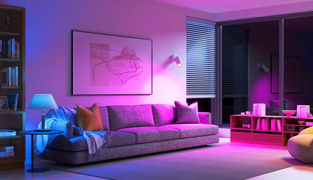 Pokój jest oświetlony fioletowymi i niebieskimi odcieniami. Widoczne są sofa, regał i okno.
