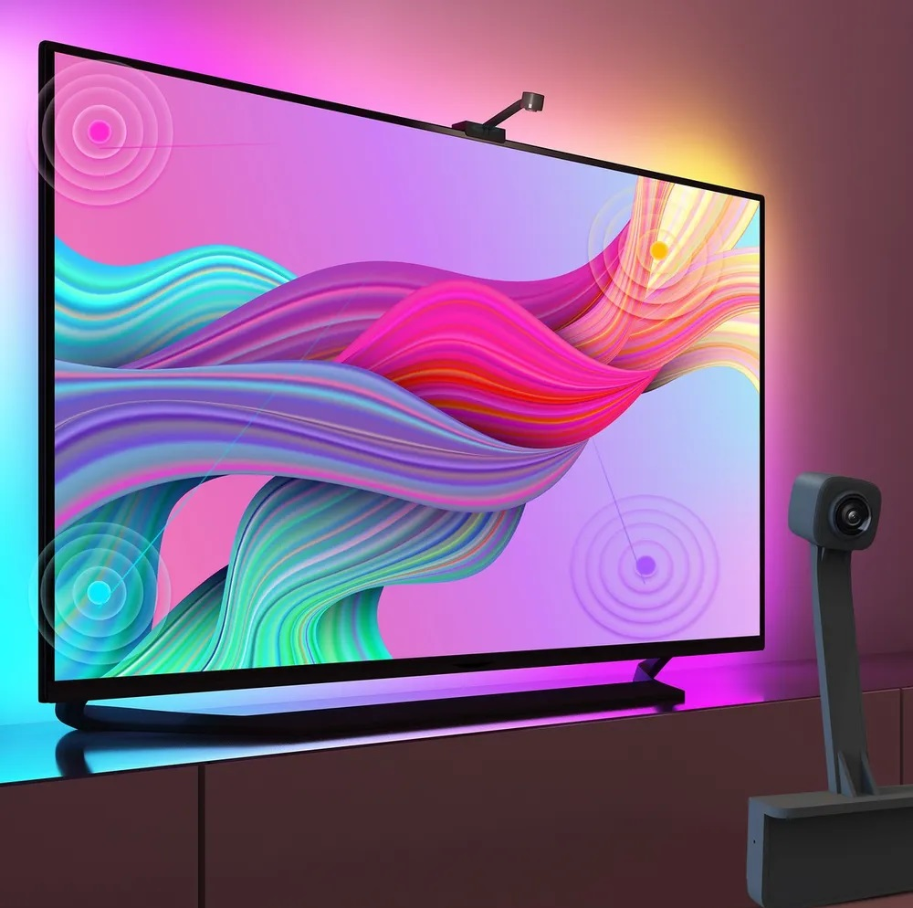 Telewizor z kolorowym wyświetlaczem, kamerą na górze i wskaźnikami fal dźwiękowych. Na szafce.