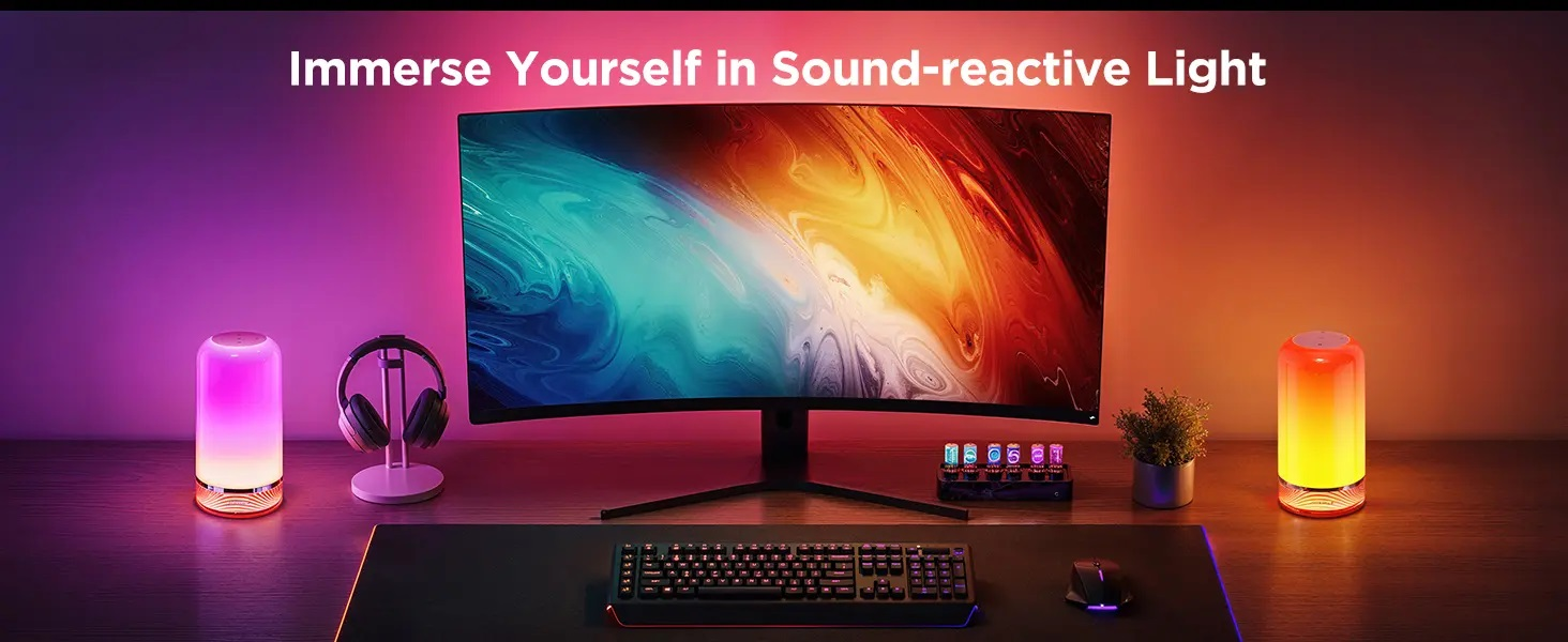 Biurko z monitorem, słuchawkami, klawiaturą, myszką i dwiema kolorowymi lampami.