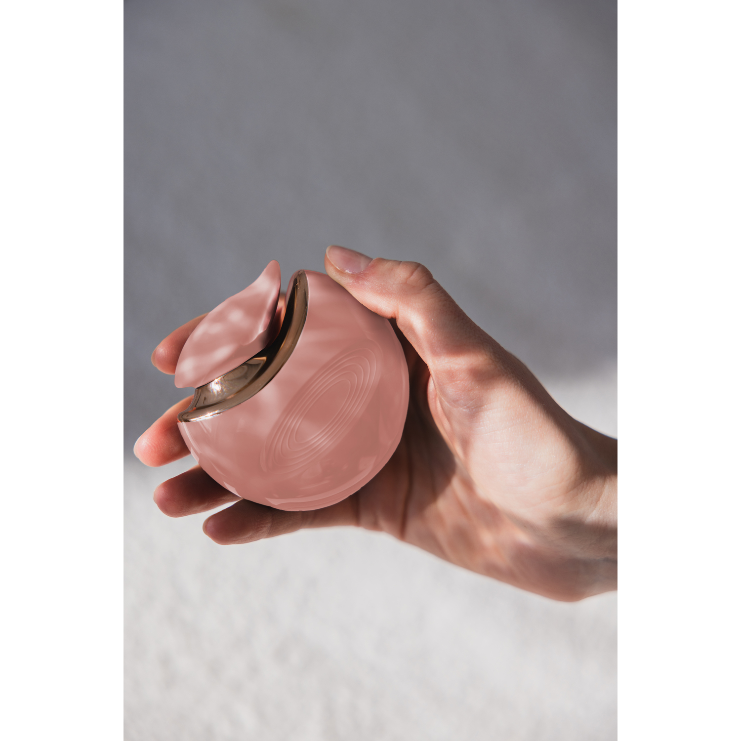 A hand holding a pink spherical beauty device.