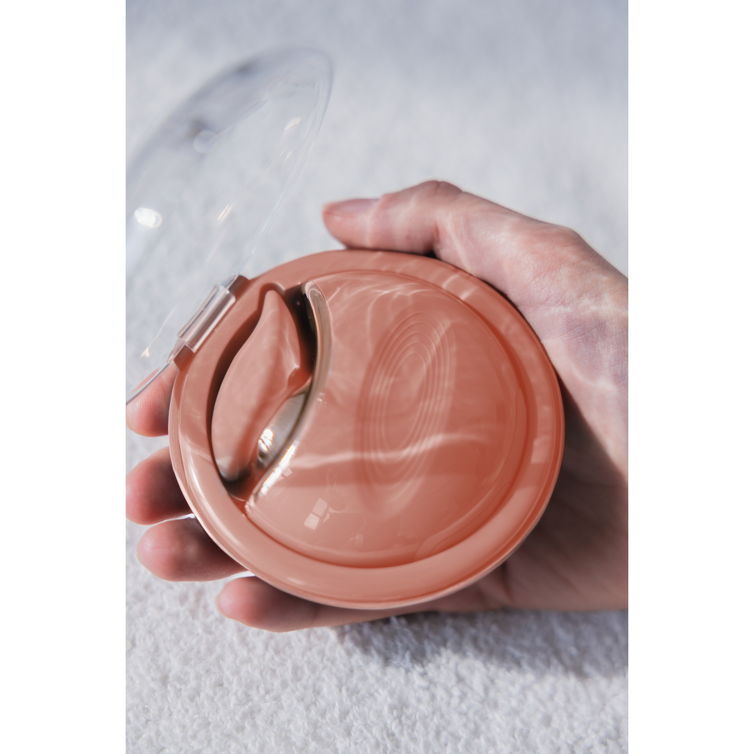 A hand holding a small, round, peach-colored face mask case.