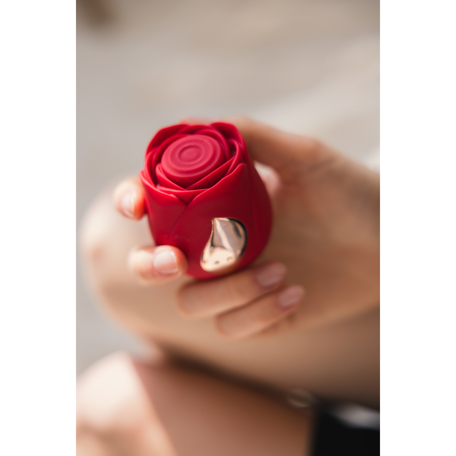 Close-up of a hand holding a red rose-shaped device. Gold accents, against a white background.