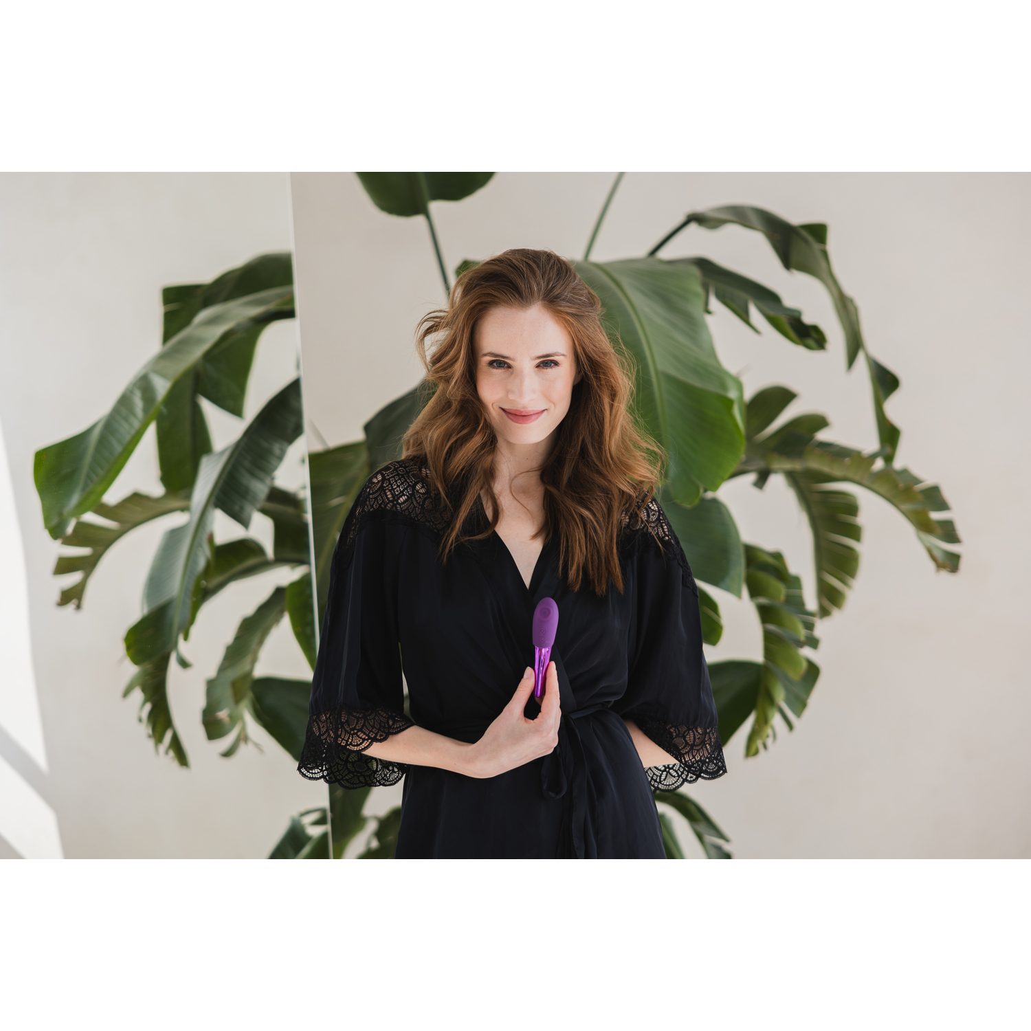 A woman in a black robe with purple sex toy smiling.