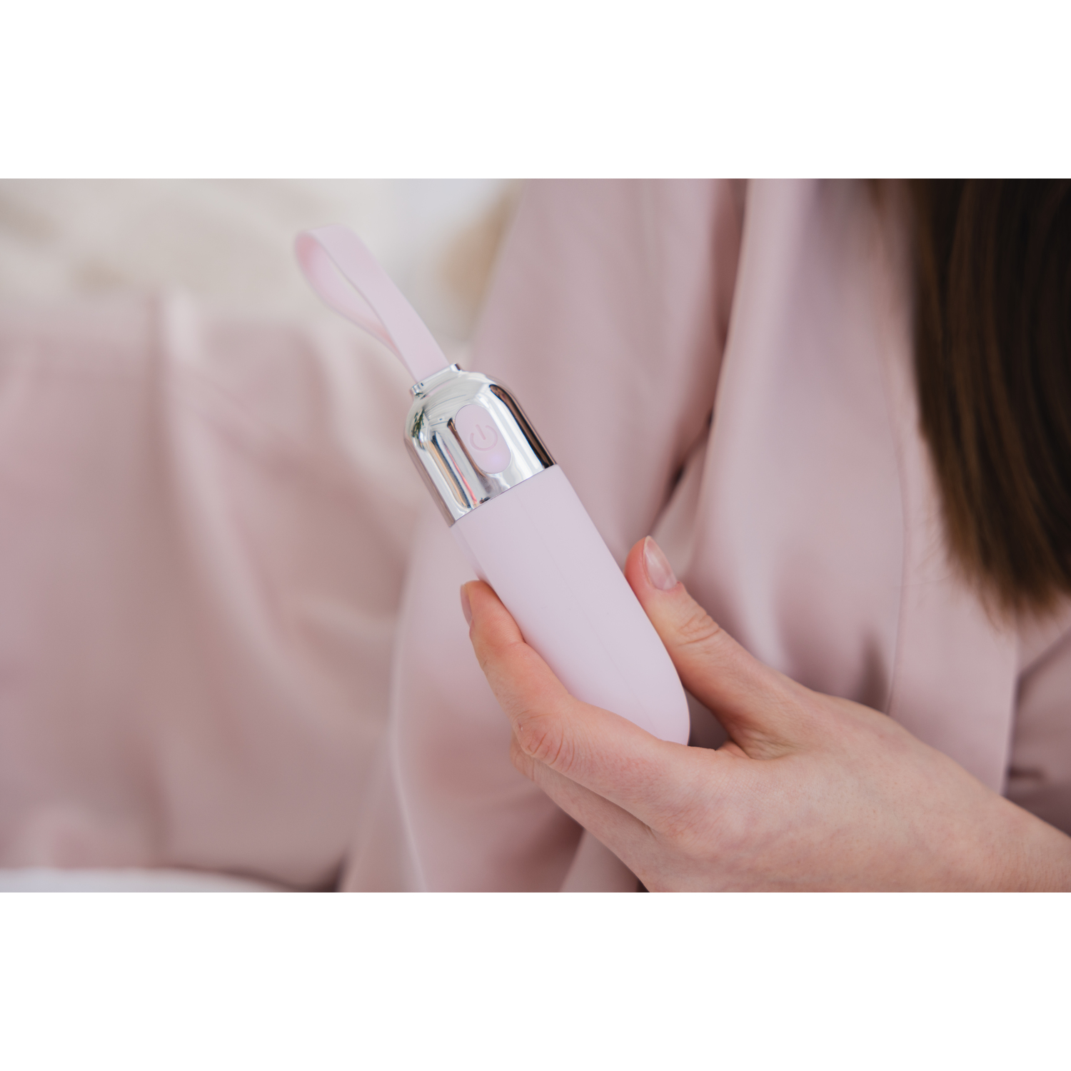 A person holding a pink, battery-operated vibrator with a silver button.