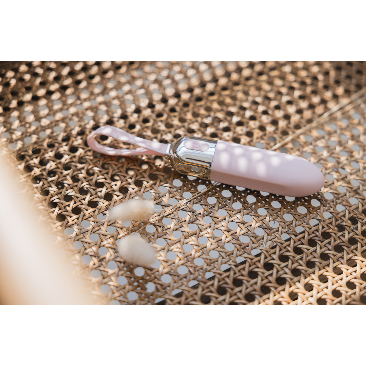 A pink vibrator rests on a wicker chair, with a pink loop and silver accents.