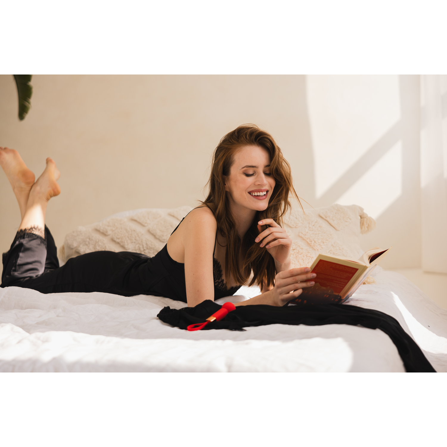 Woman lying on bed reading a book, smiling.