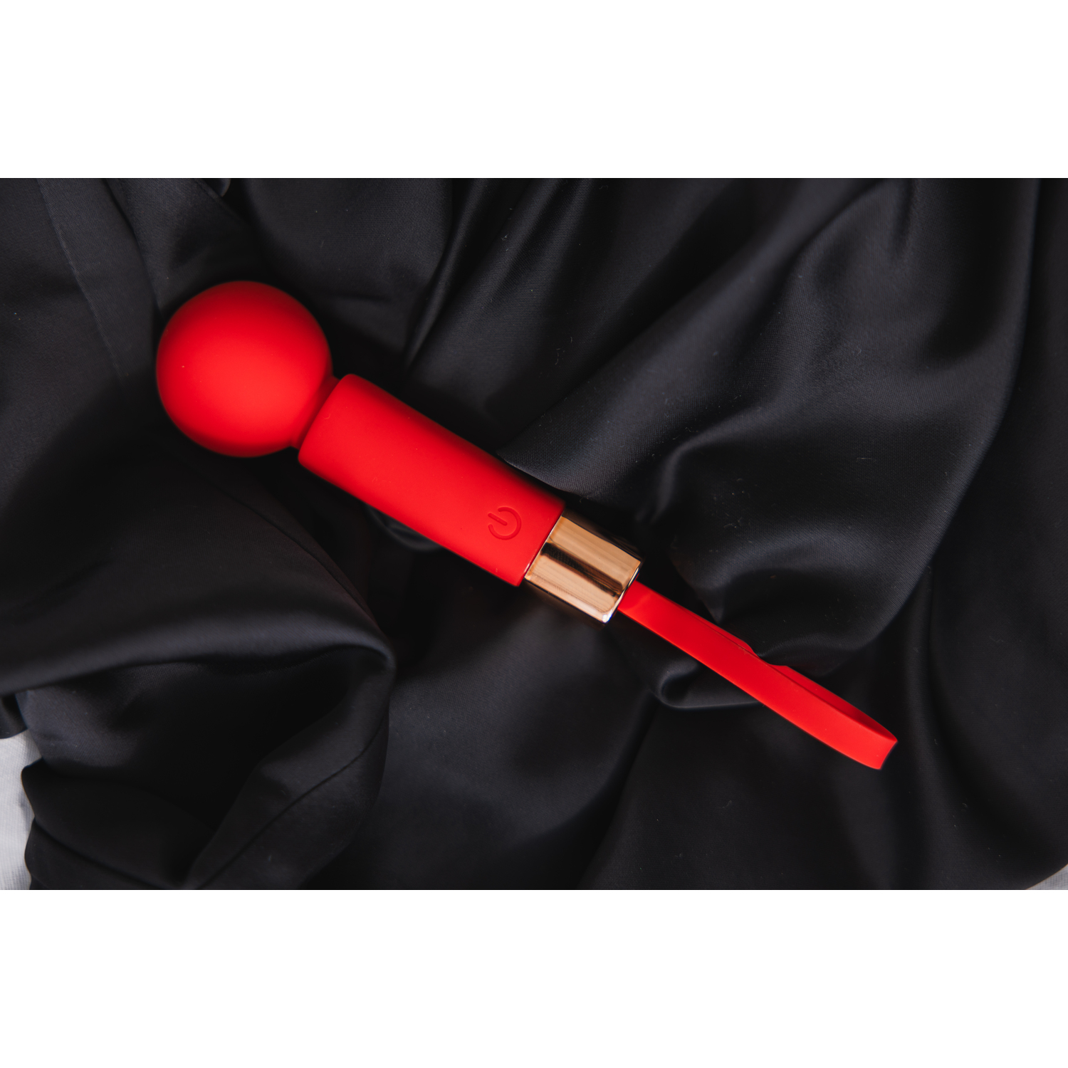 Red sex toy on black fabric. A ball on top, and a loop on the bottom.