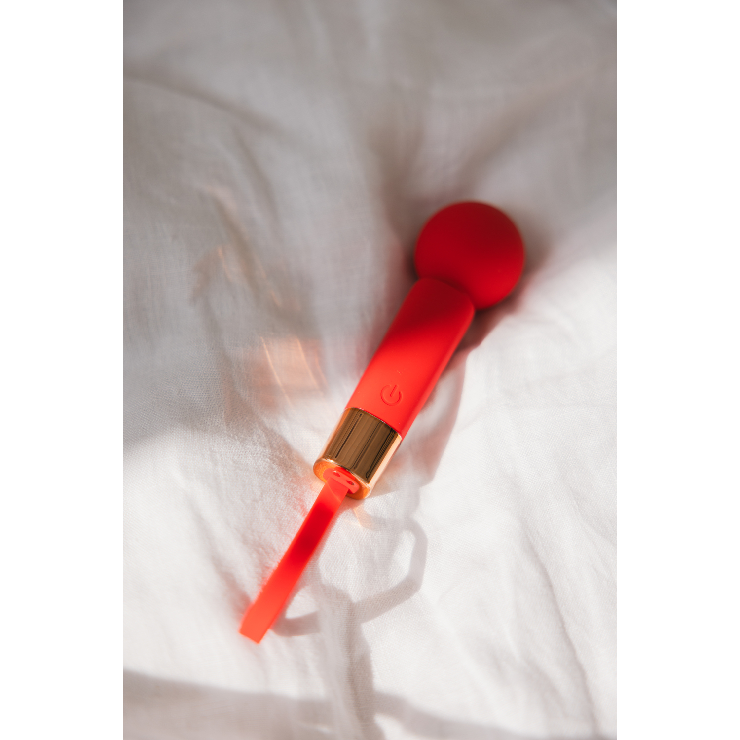 Red vibrator on white fabric. Gold accents and a power button.