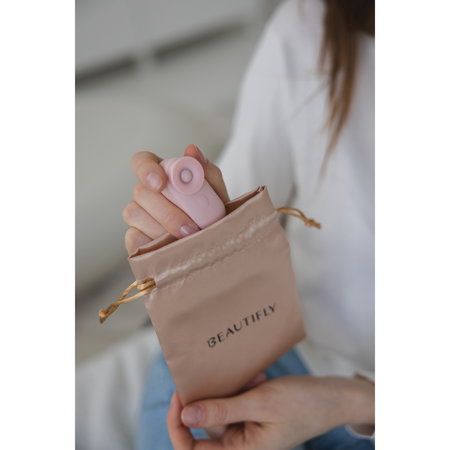 A person holding a pink sex toy in a beige fabric bag with the word BEAUTIFLY on it.