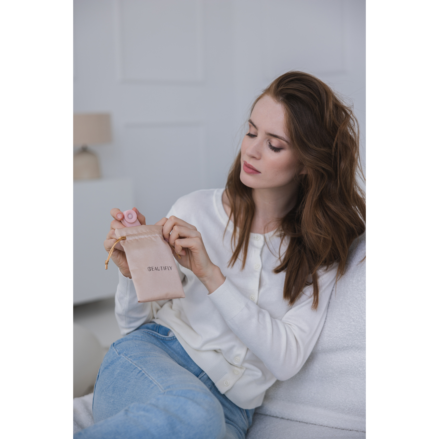 Woman holding a small pouch with a menstrual cup and a pink object. White room.