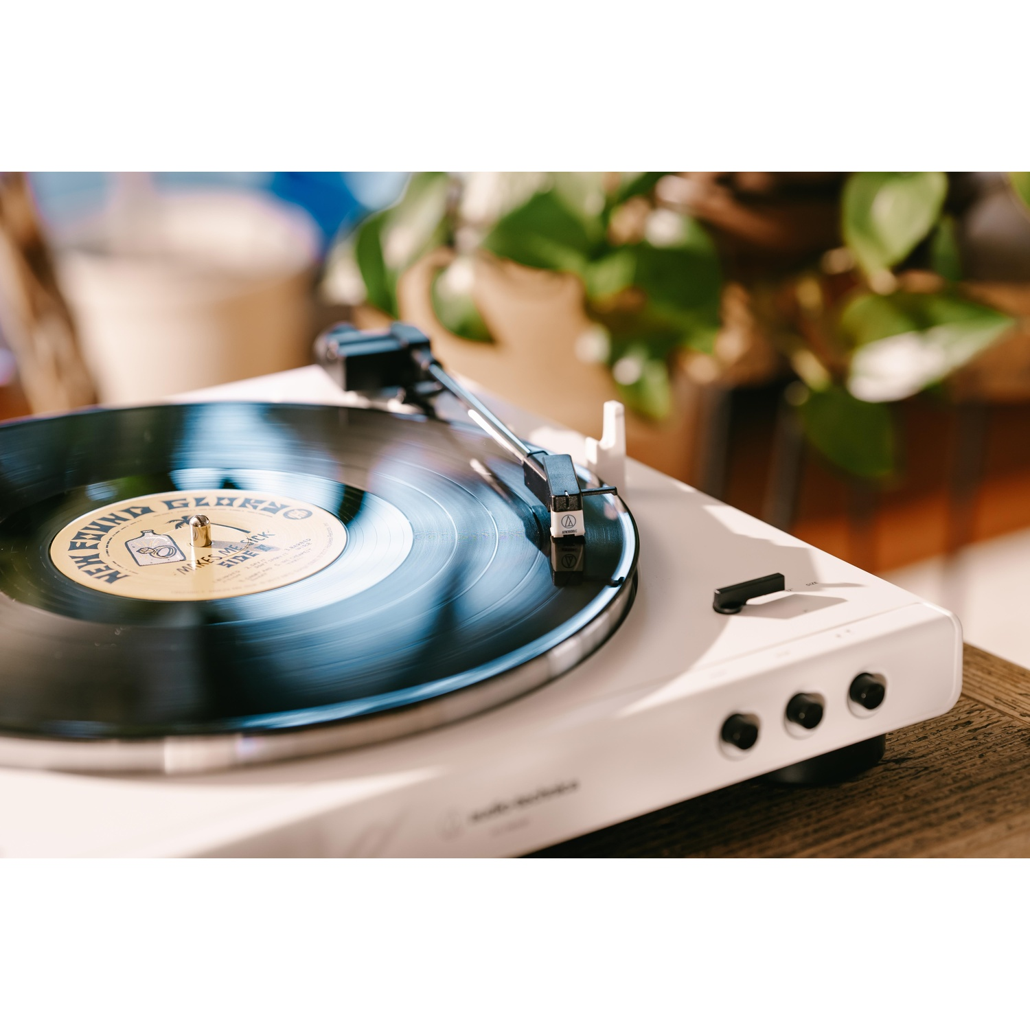Un giradischi bianco con un disco in vinile in riproduzione. Lo sfondo mostra una pianta e una finestra.