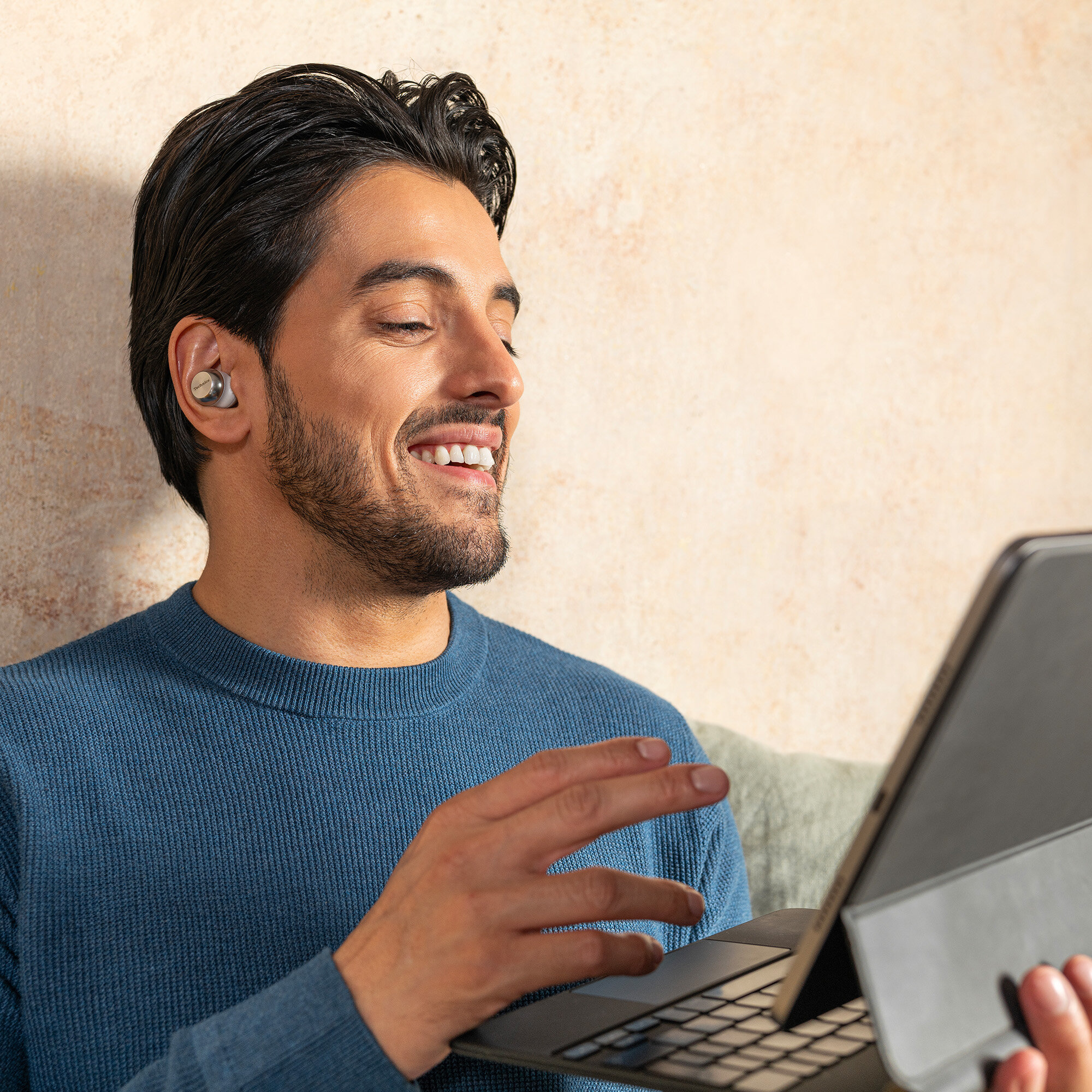 Mężczyzna w słuchawkach, uśmiechnięty, patrzy na tablet z klawiaturą.