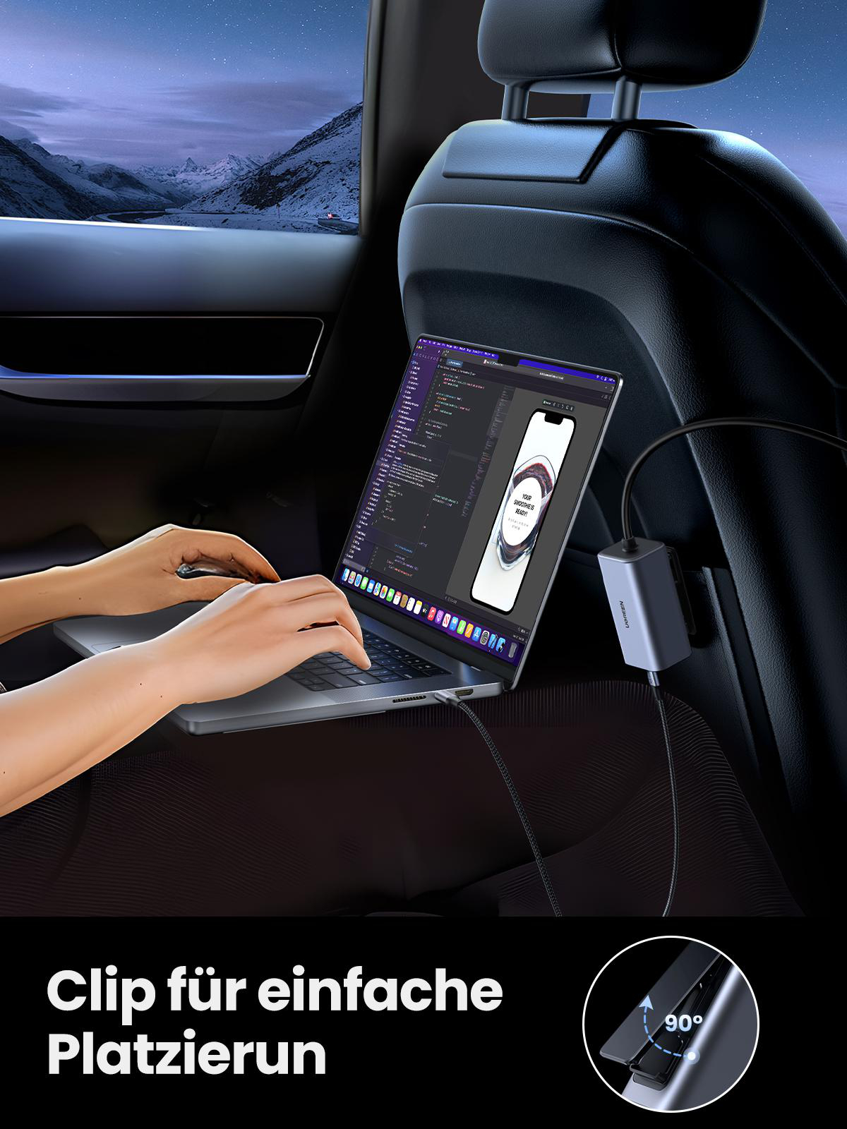 Ein Laptop liegt auf dem Schoß einer Person in einem Auto und ist mit einem Gerät verbunden. Eine Berglandschaft ist zu sehen.