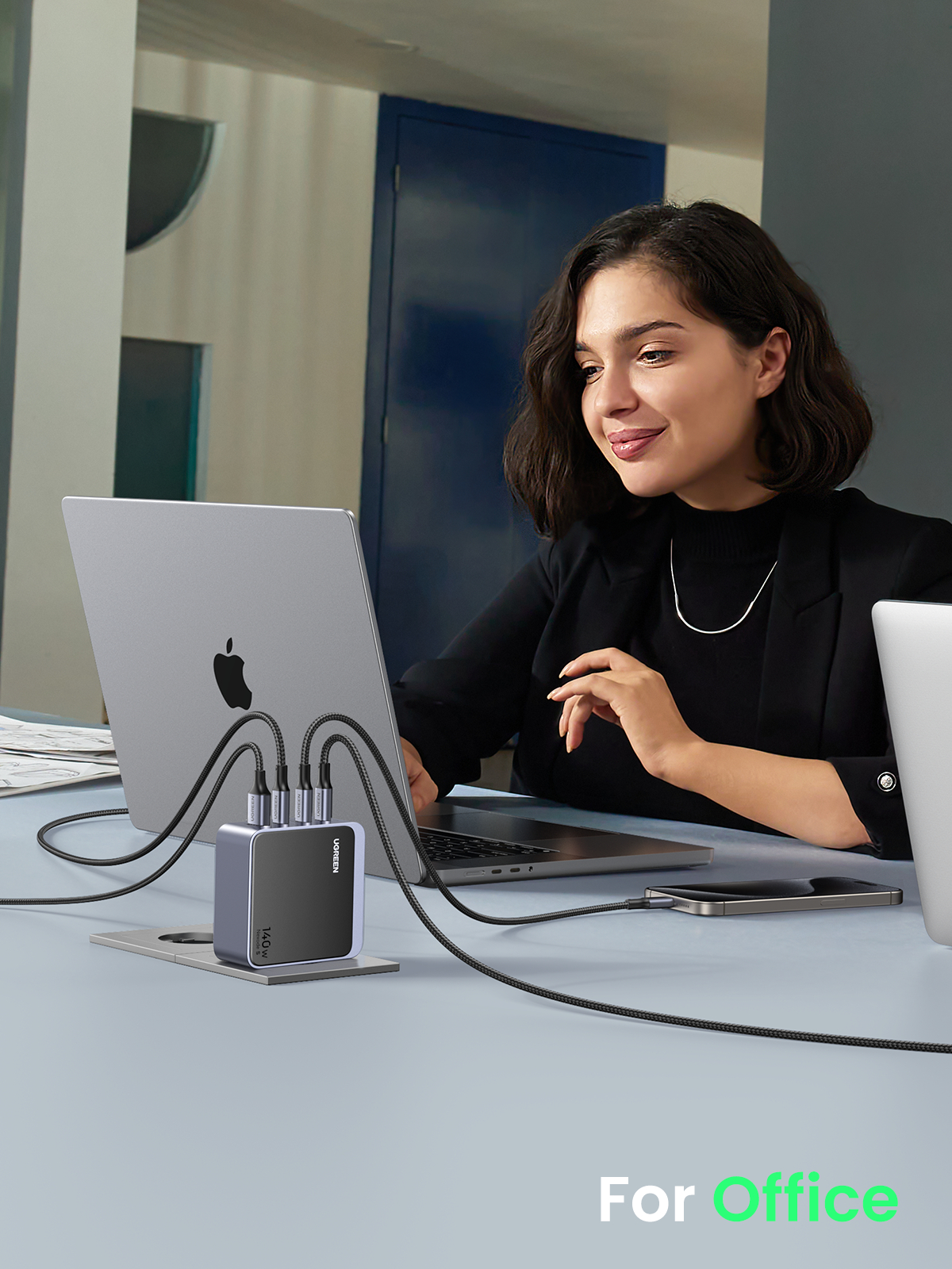 Frau am Schreibtisch benutzt Laptop. Mehrfach-Port-Ladegerät speist Geräte.