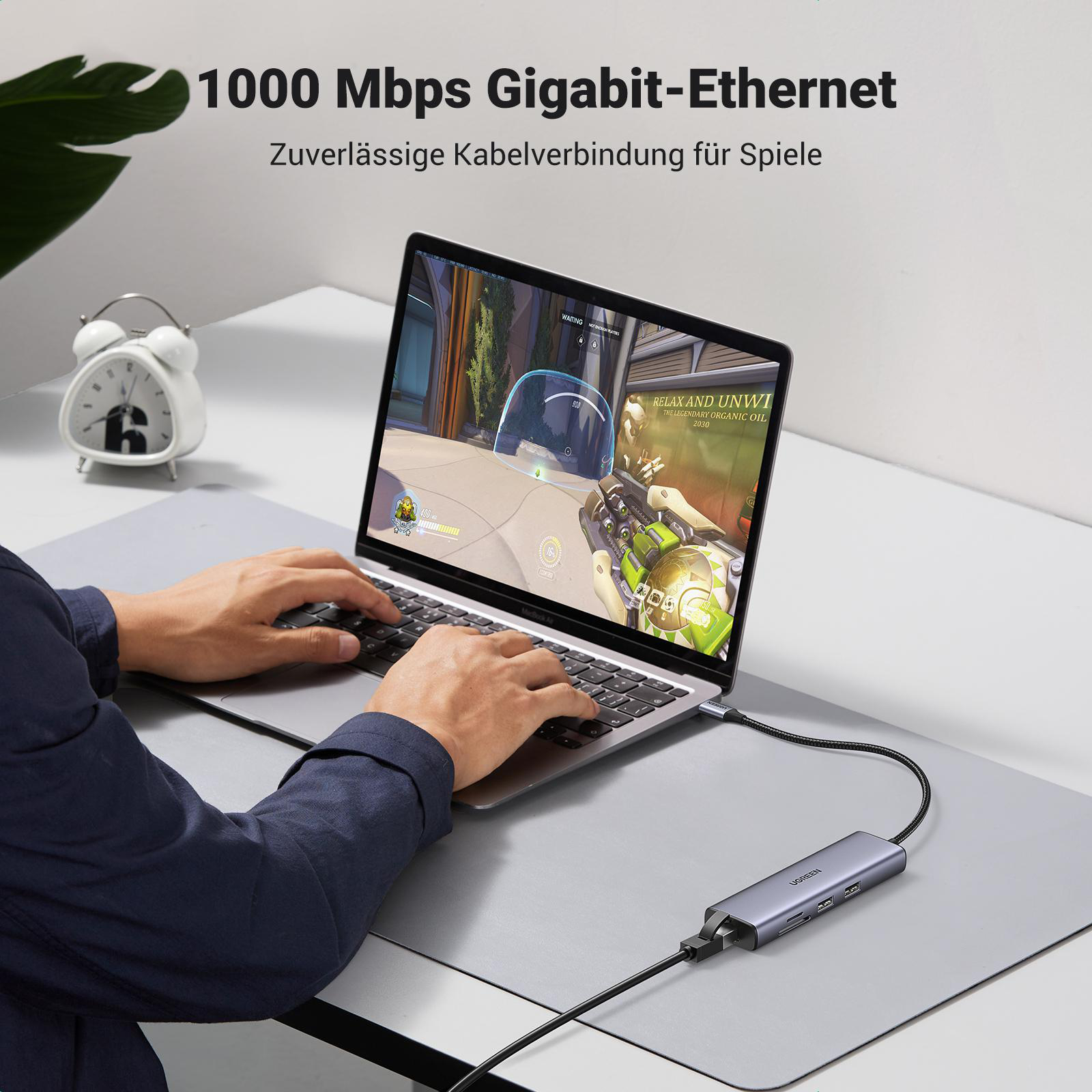 Eine Person, die einen Laptop mit angeschlossenem Hub auf einem grauen Schreibtisch benutzt.