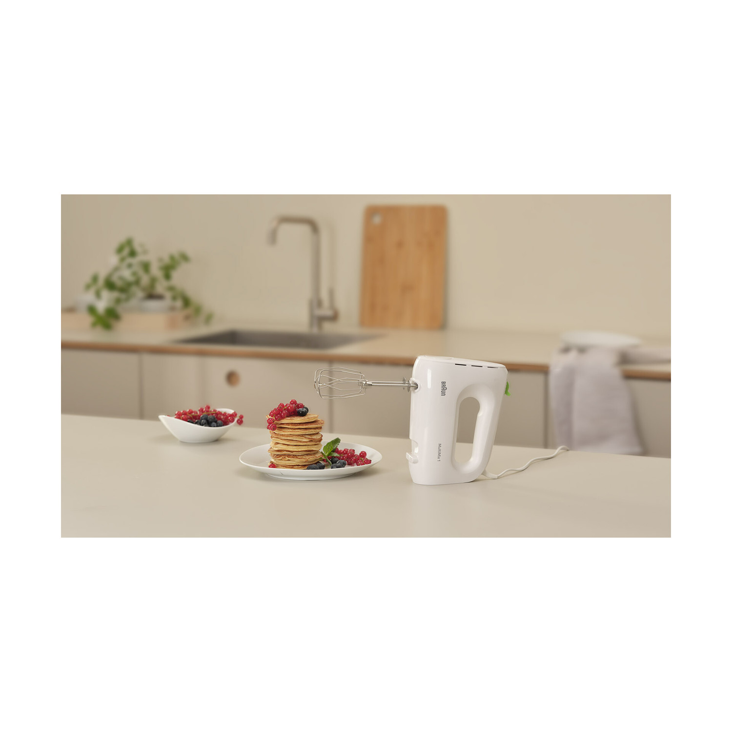 Un frullatore a mano bianco con pancake, frutta in una cucina.