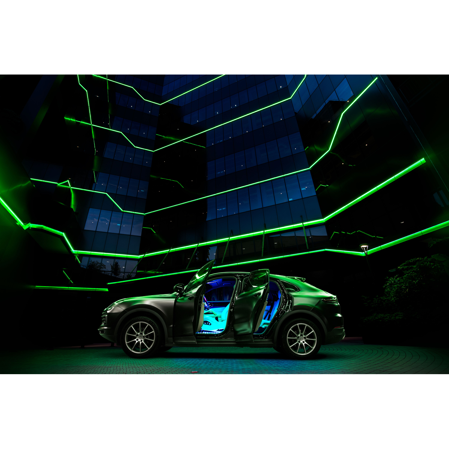 A green car with open doors parked in front of a modern building with green lights.