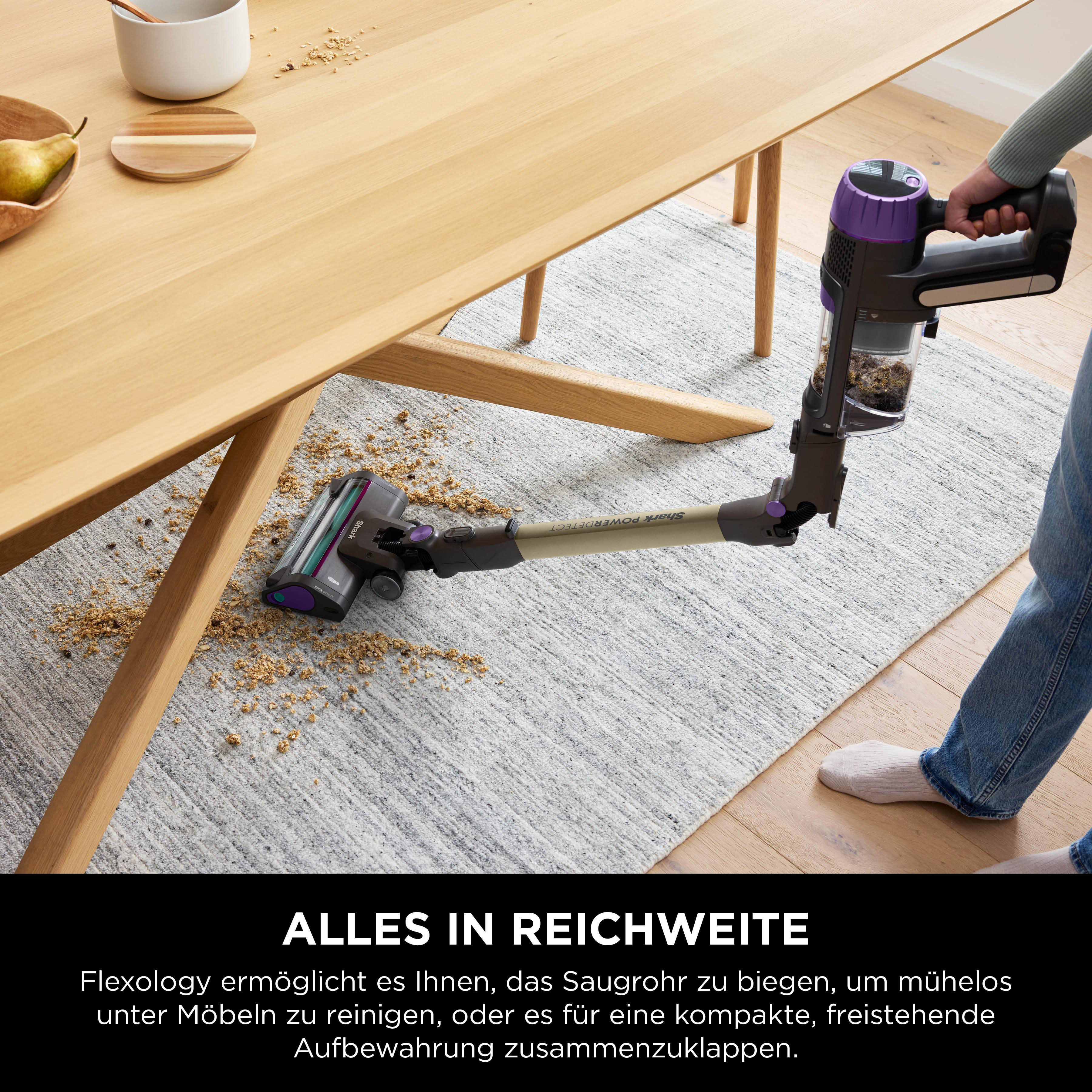 Eine Person, die einen Teppich mit einem Staubsauger saugt, Holztisch im Hintergrund.