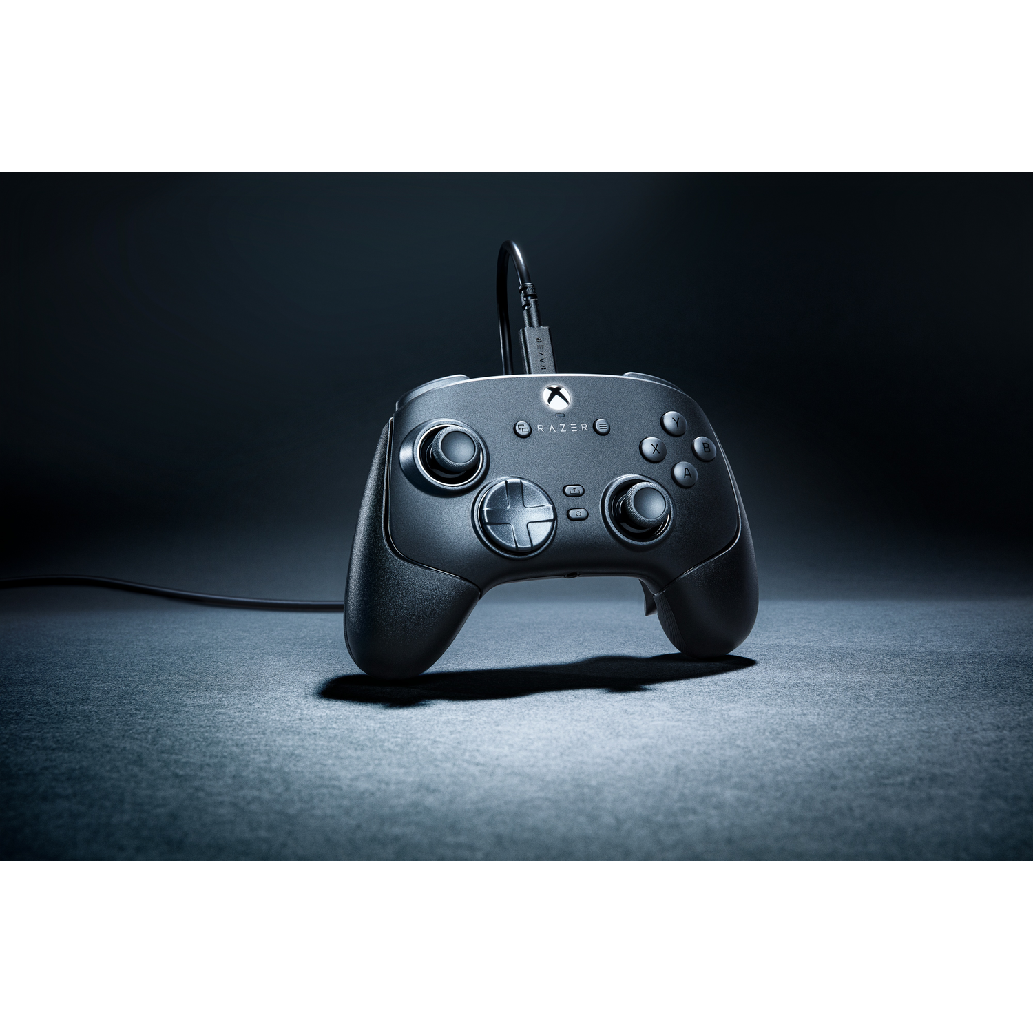 A black game controller with buttons and a Razer logo on a dark surface. A cable is connected.