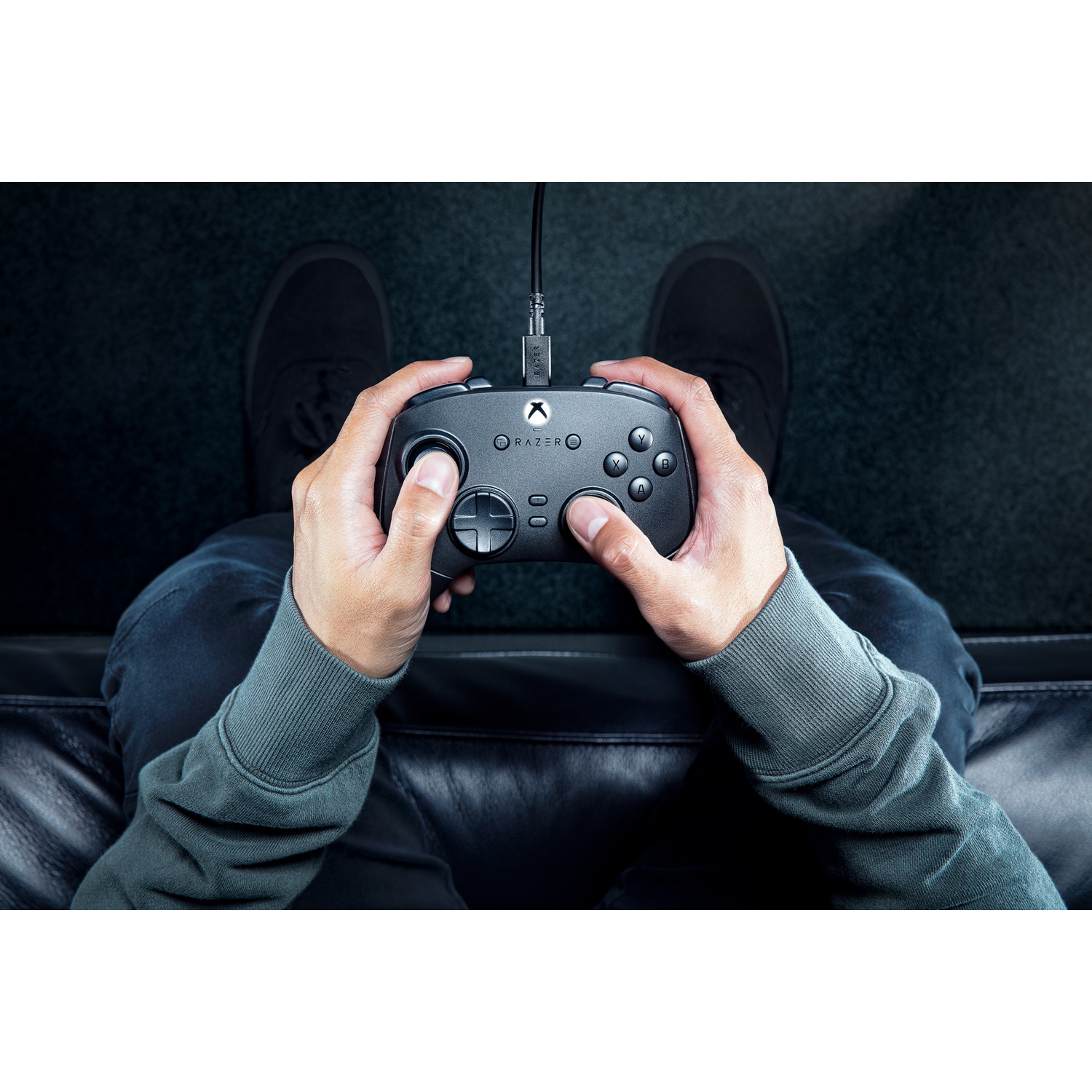 Hands holding a black Razer controller, connected by a cable, on a couch.