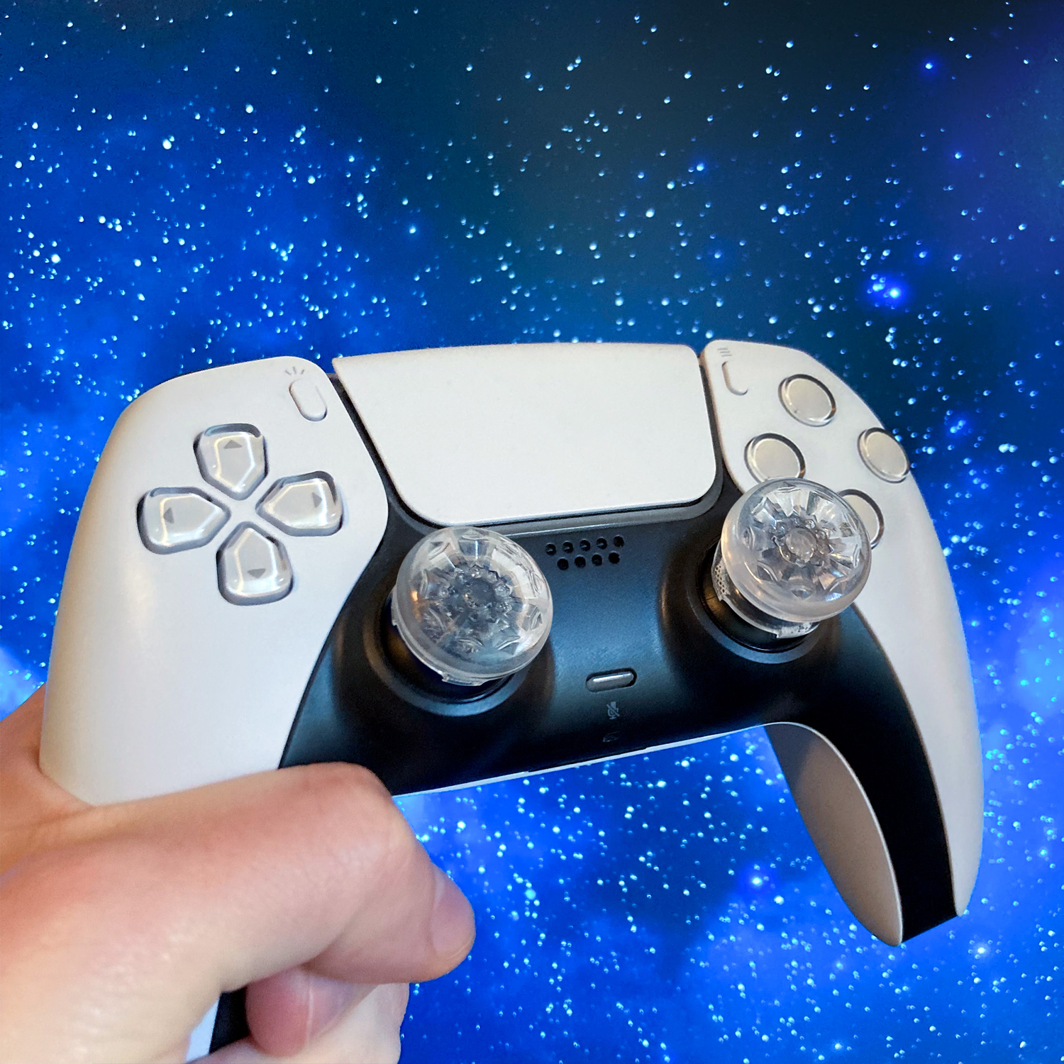 Witte en zwarte PS5-controller in een hand, met een sterrenblauwe achtergrond.
