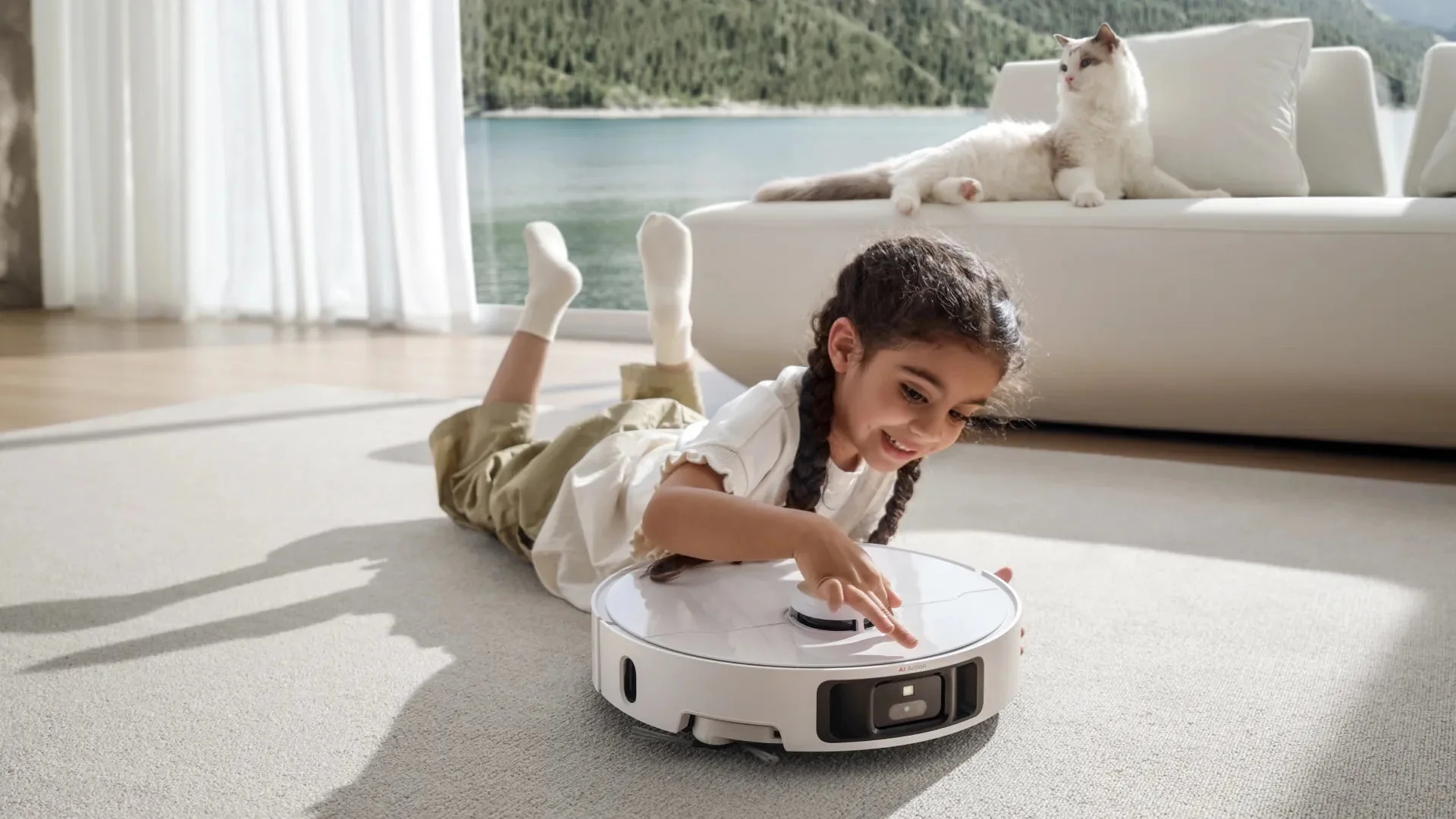 Lány robot porszívóval játszik. Macska a kanapén. Napos szoba.
