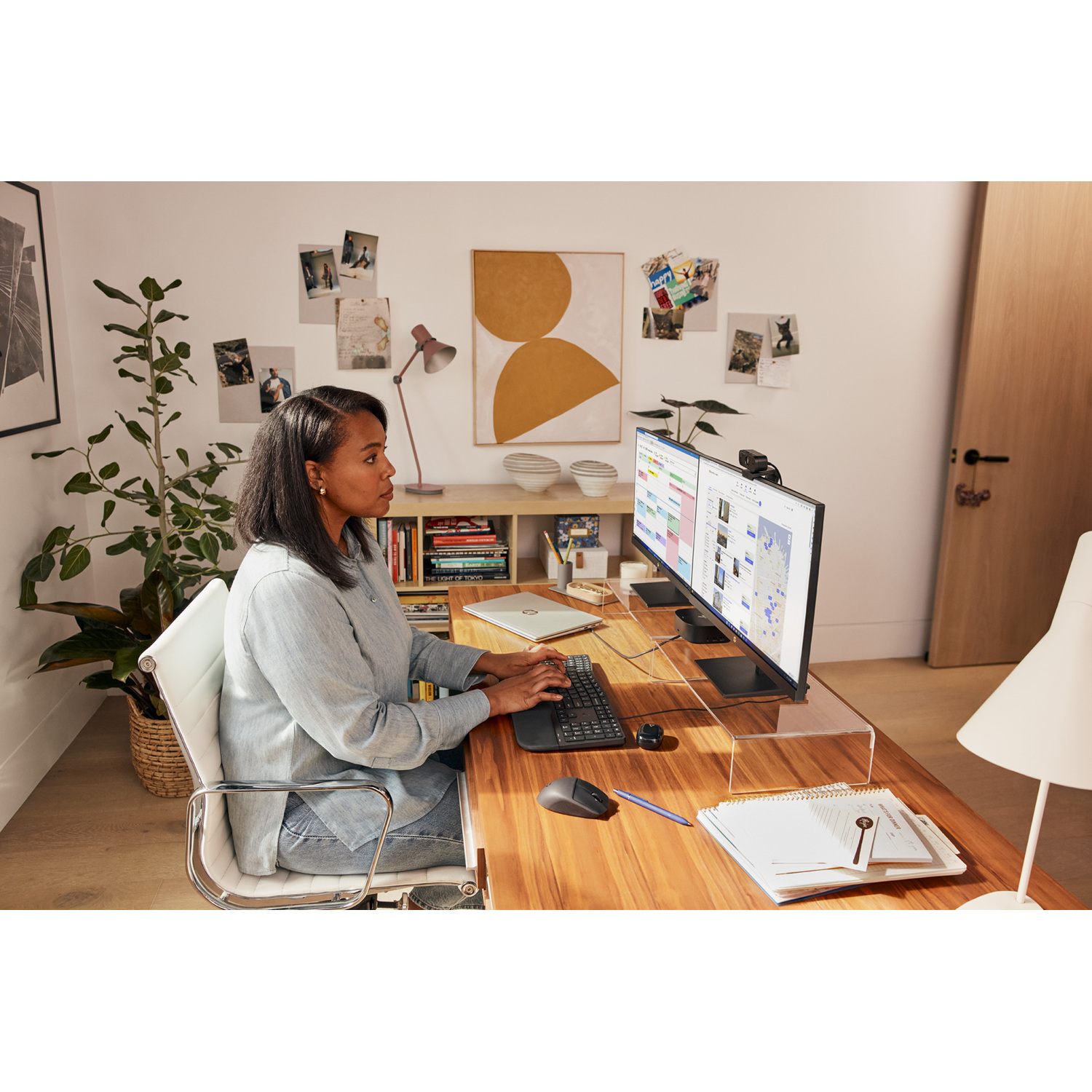 Femme à un bureau avec deux moniteurs, une souris, un clavier et divers articles de bureau.