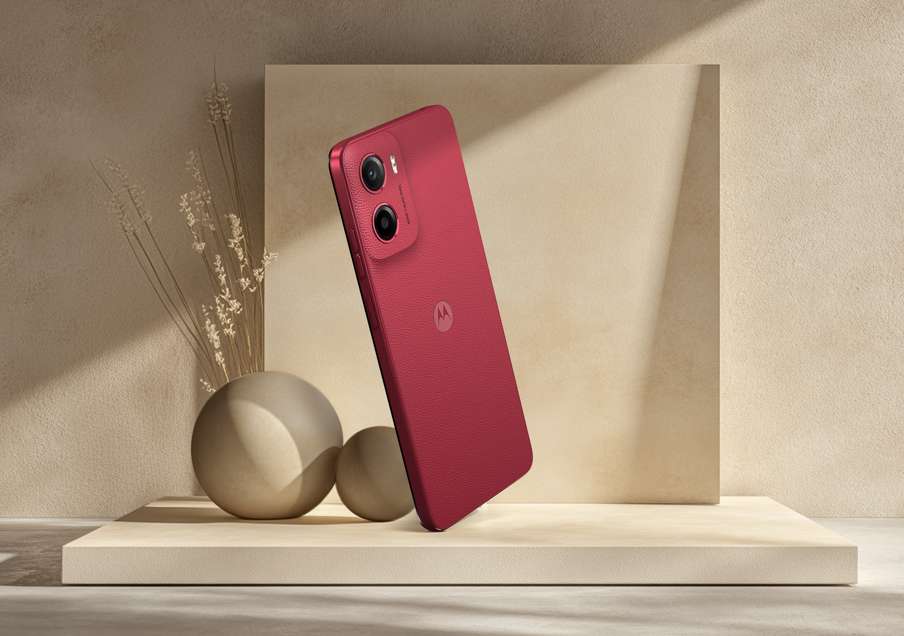 Czerwony smartfon na beżowej powierzchni. Obok dwie kule i roślina.