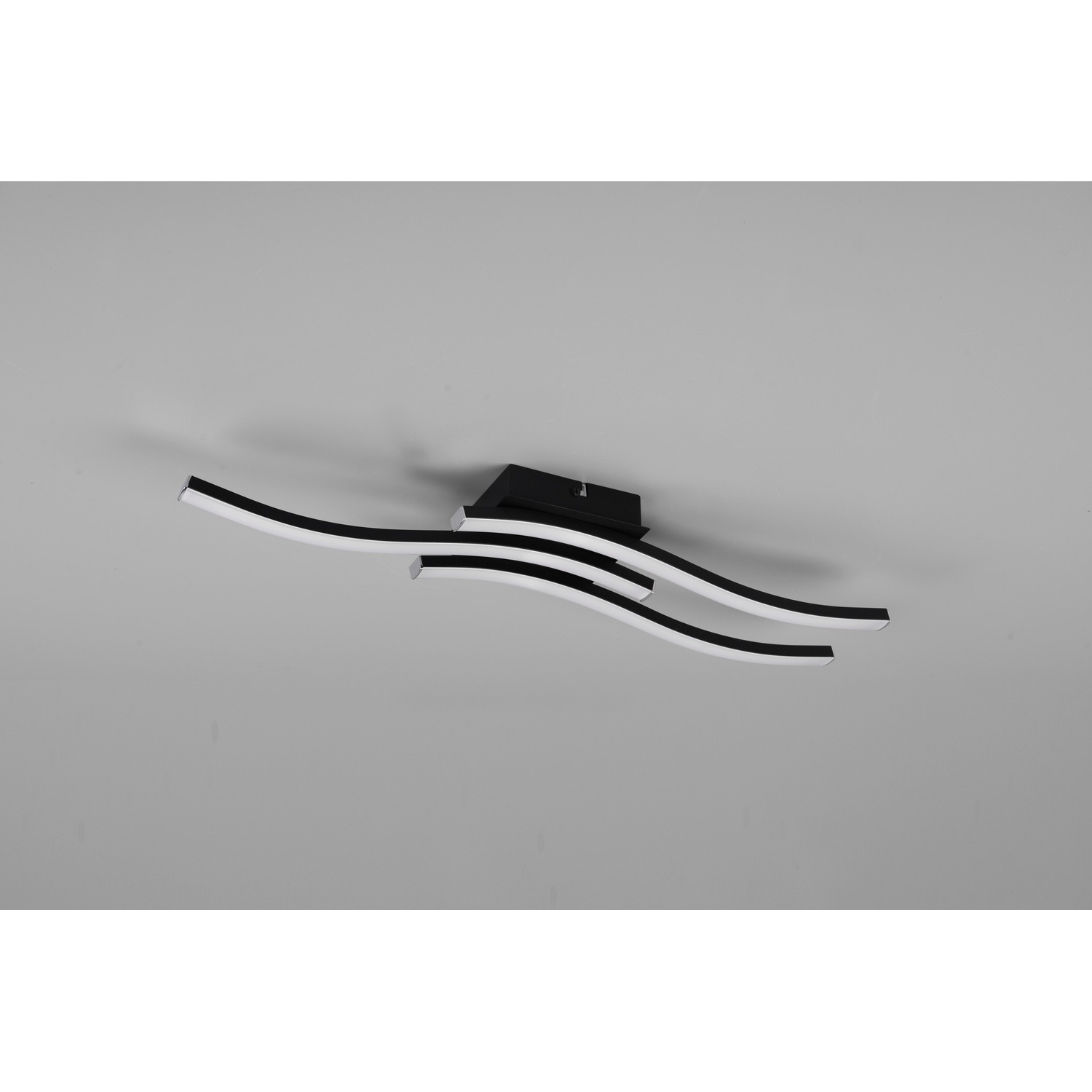 Lampada da soffitto con tre strisce LED nere curve e luce bianca su superficie grigia.
