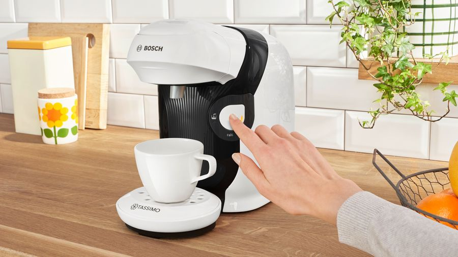 Una mano presiona un botón en una cafetera blanca y negra, junto a una taza.