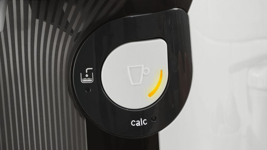 Panel de control de la cafetera. Icono de taza blanca con arco de luz amarillo. Panel negro con texto 'calc' e icono de agua.