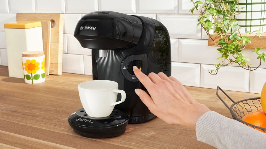 Una persona está utilizando una cafetera negra Bosch Tassimo con una taza blanca.