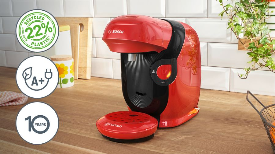 Cafetera Tassimo Bosch roja con base negra, sobre superficie de madera. Etiquetas ecológicas.