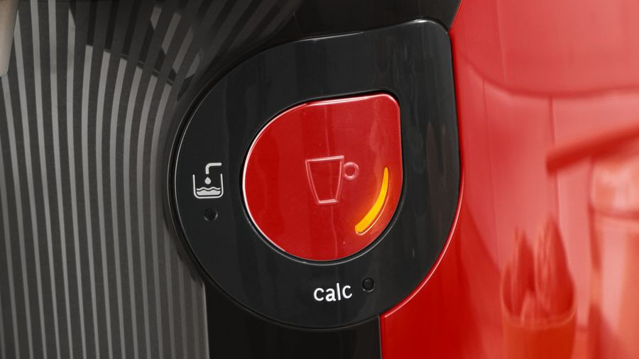 Primer plano de un botón rojo en una cafetera, con la palabra calc y símbolos de agua/taza.
