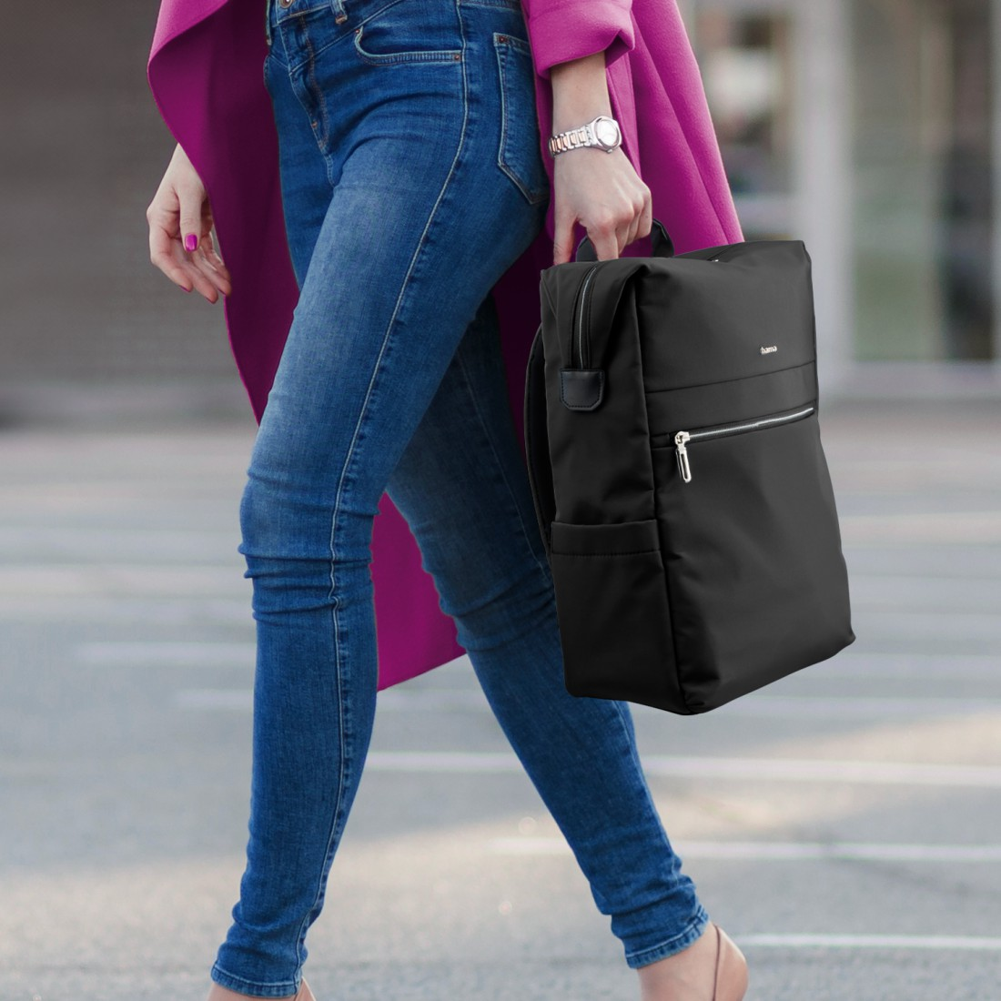 Eine Frau in Jeans, mit einem schwarzen Rucksack und einem pinken Mantel.