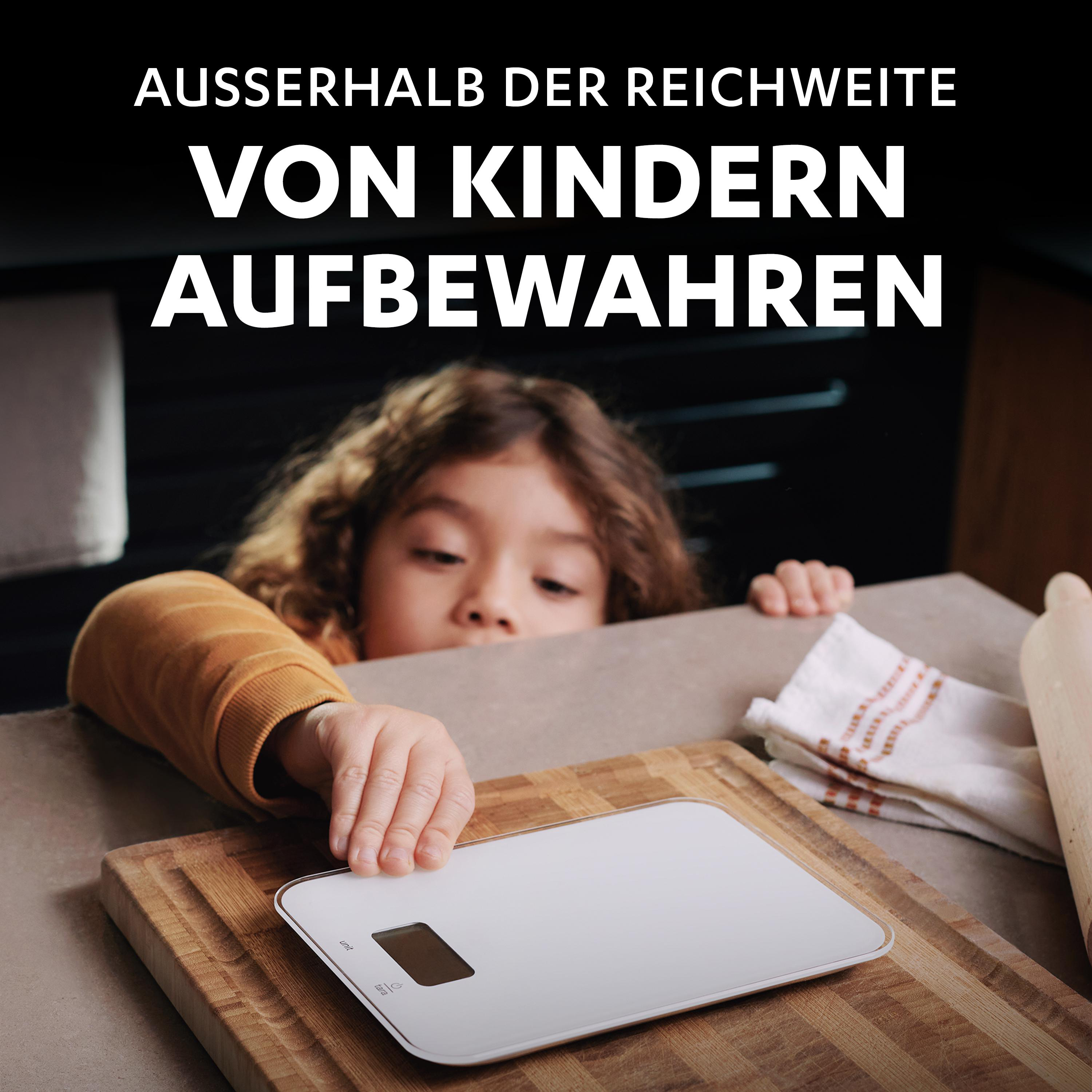 Ein Kind, das nach einer weißen Waage auf einem hölzernen Schneidebrett greift.