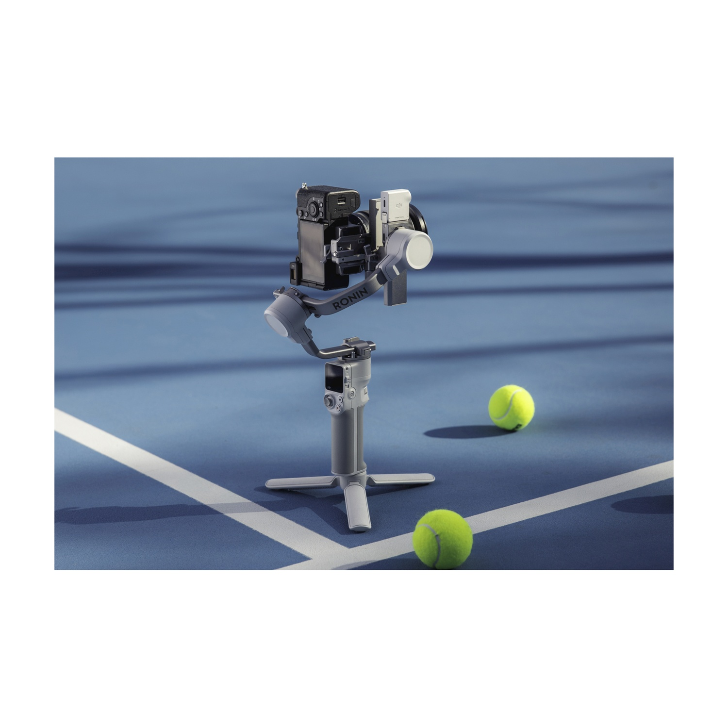 Uno stabilizzatore per fotocamera su un treppiede, con due palline da tennis su un campo blu. La fotocamera è montata sullo stabilizzatore.