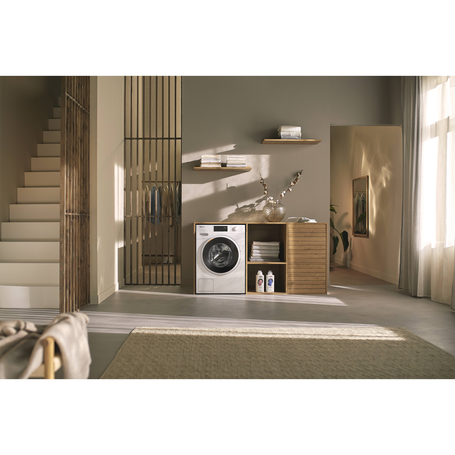 Een moderne wasruimte met een wasmachine, houten planken en een tapijt. Natuurlijk licht komt binnen.
