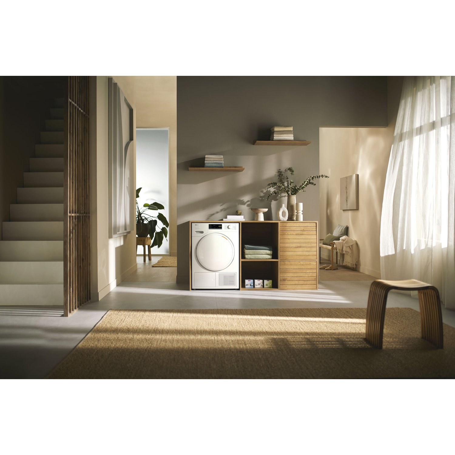 A well-lit entryway with stairs, a cabinet with a dryer, and a rug.