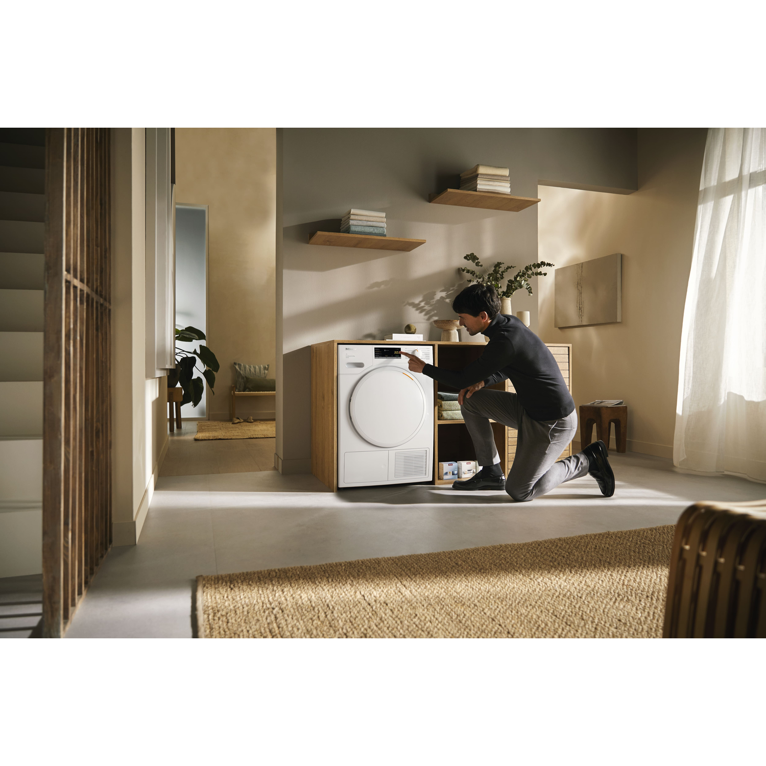 A man kneeling in a modern room, interacting with a washing machine.
