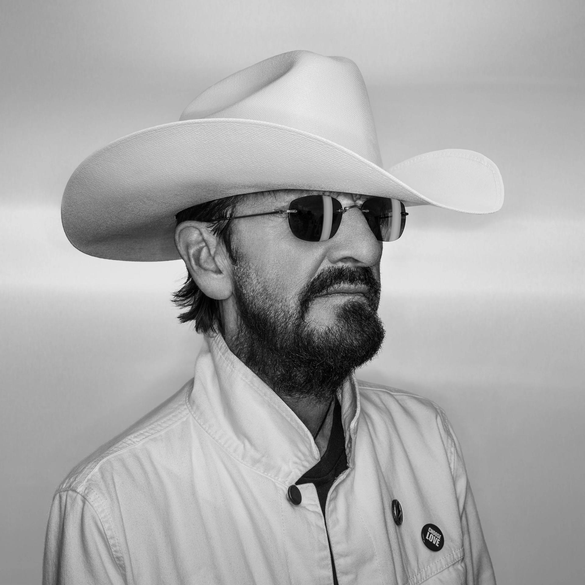 Ein Mann mit Cowboyhut, Sonnenbrille, Bart und Jacke in Schwarzweiß.