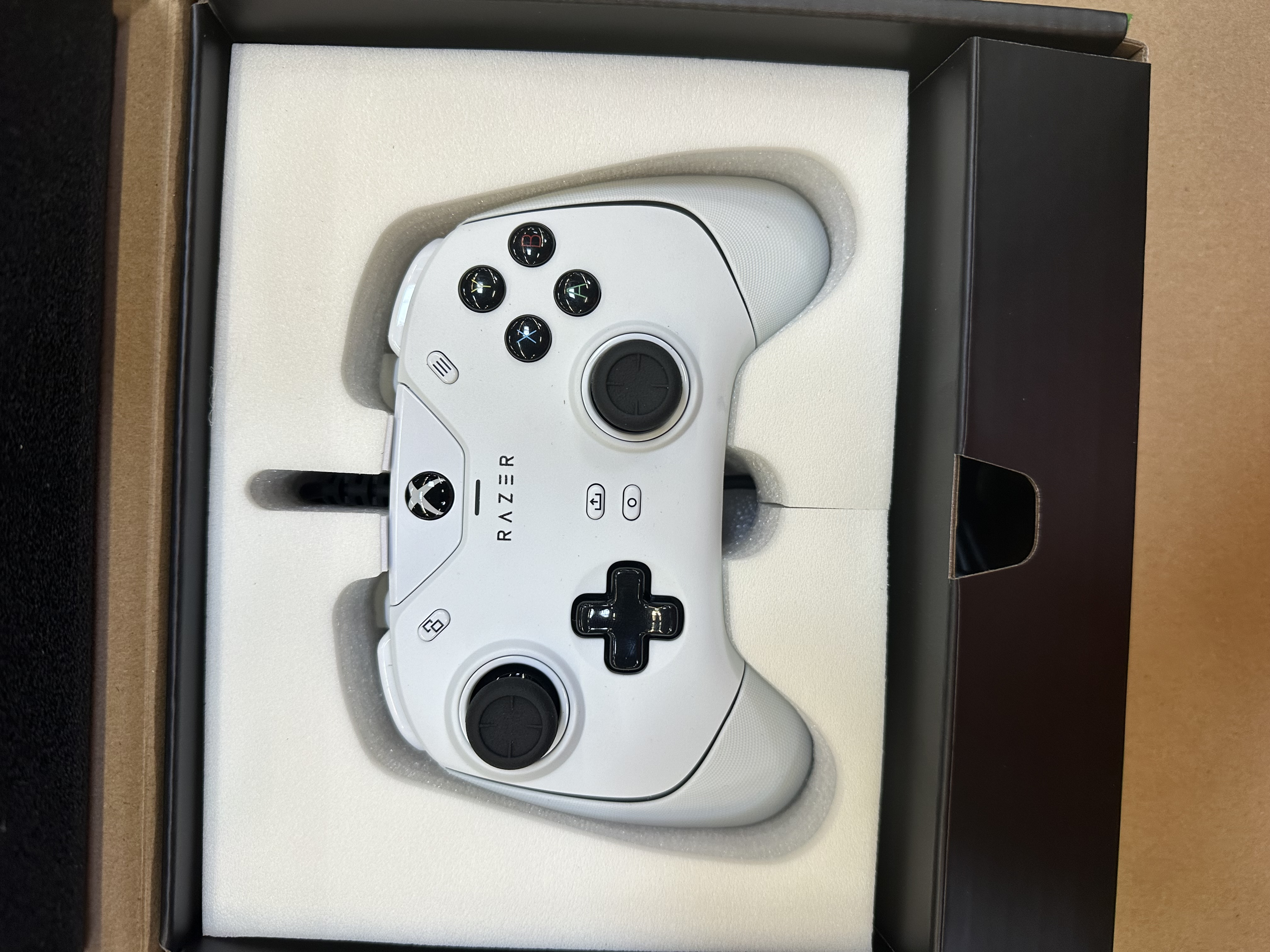 Biały kontroler Razer w pudełku, widok z boku, widoczne przyciski.