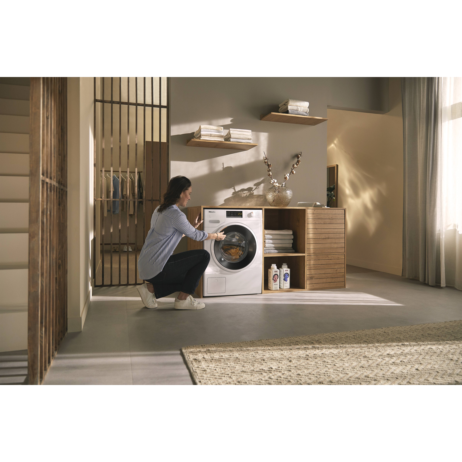 A woman is using a white washing machine. The machine door is closed. Background is a room.