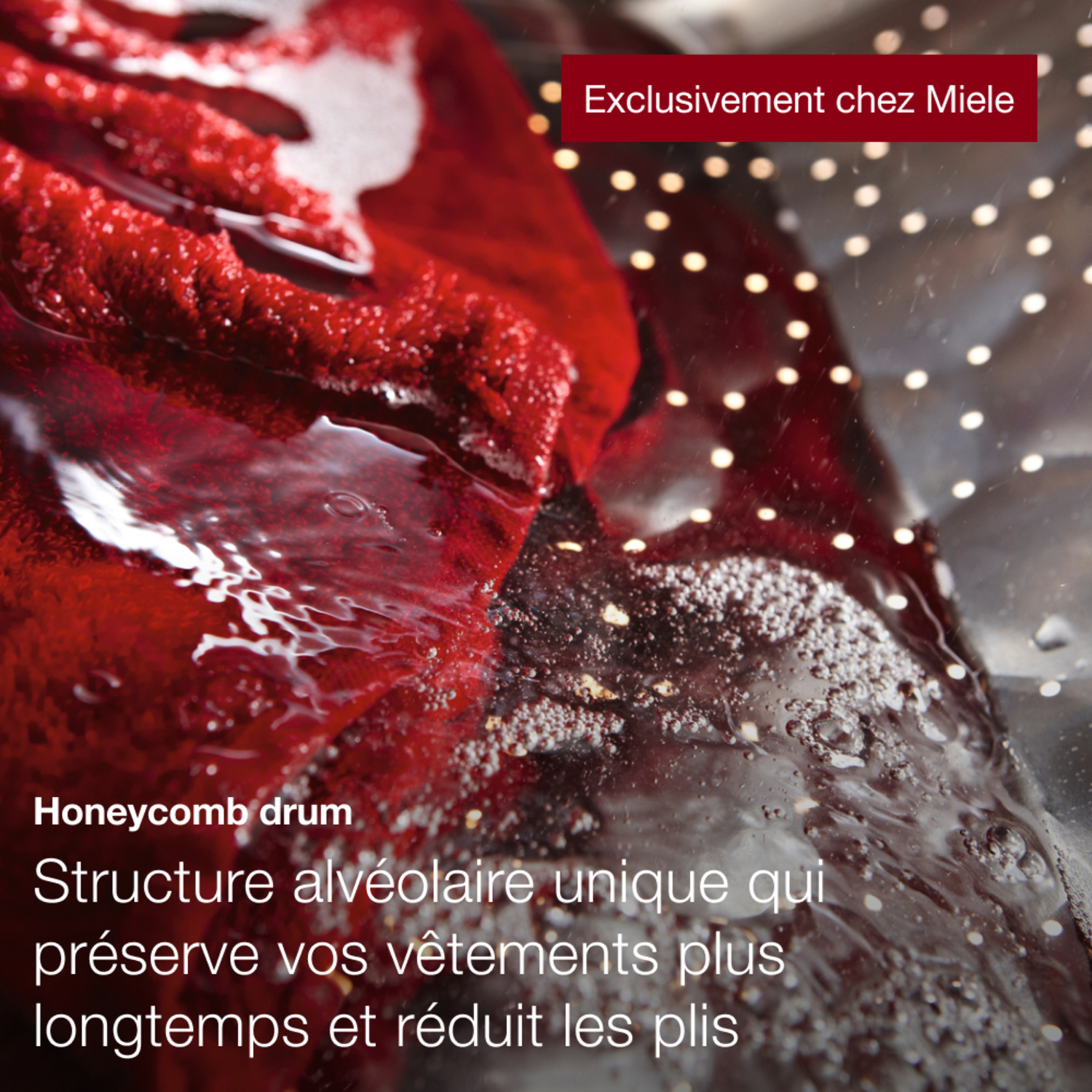 Tambour de machine à laver avec des vêtements rouges dans l'eau. Bulles et structure en nid d'abeille visibles.