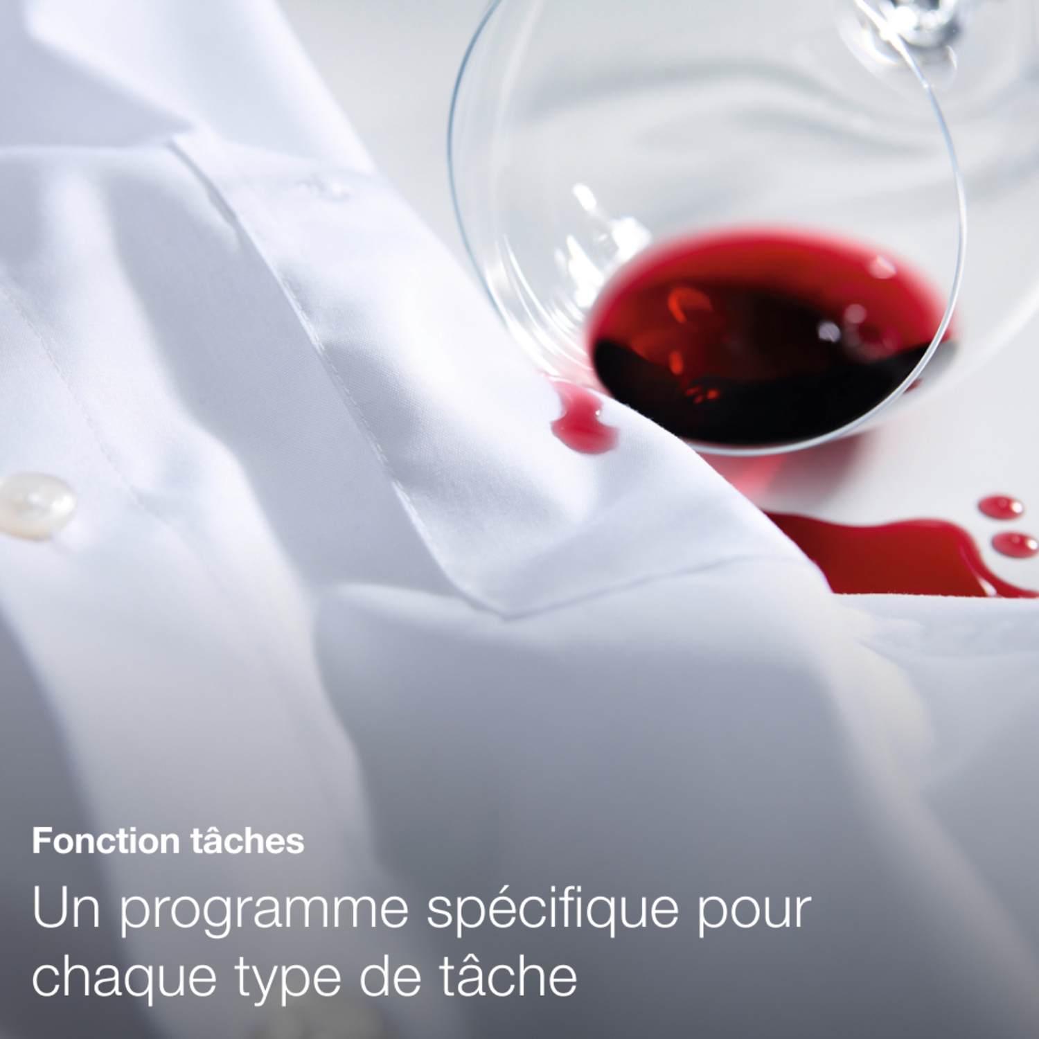 Chemise blanche avec tache de vin rouge. Un verre de vin est au-dessus, incliné, avec du liquide rouge.