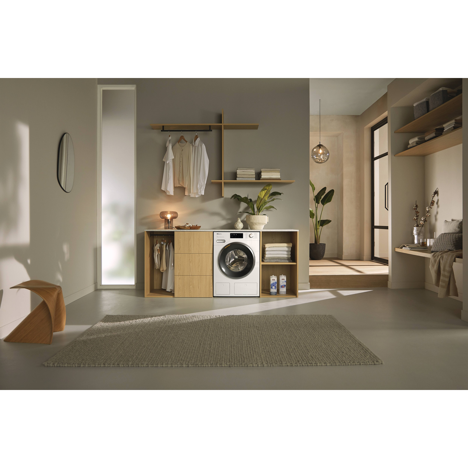 Laundry room: washer, wooden shelves, plants, rug, hanging clothes, and a window with natural light.