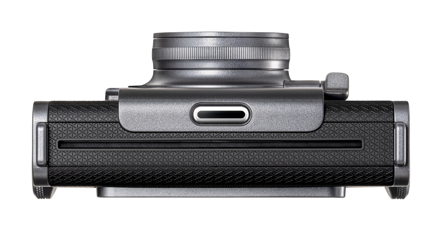 Top view of a black camera with a silver top. It has a brown strap.